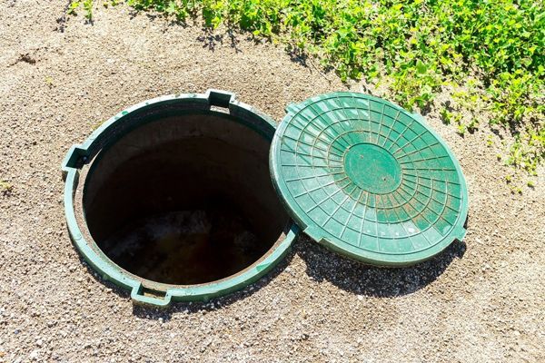 A green manhole cover is sitting on top of a dirt field.