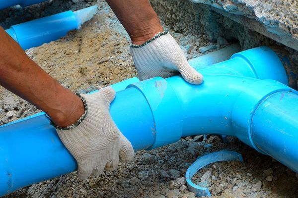 A person wearing gloves is working on a blue pipe