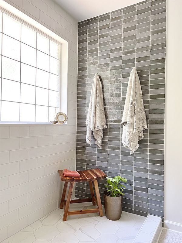 A bathroom with two towels hanging on the wall and a stool.