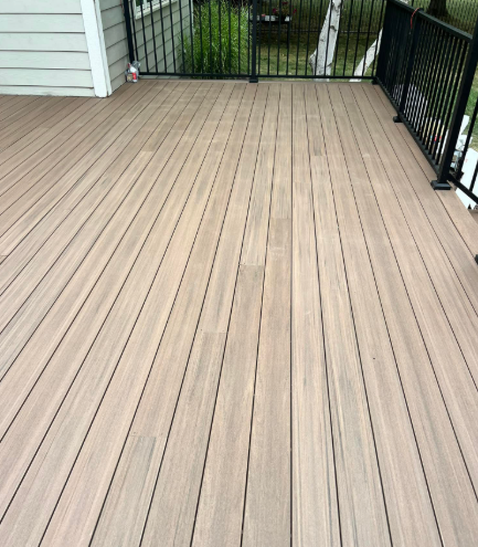 Brown composite deck with black railing and siding in the background.