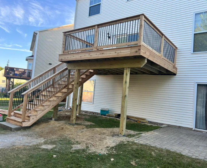 A wooden deck with stairs attached to a two-story white house. Black railings border the deck and stairs.