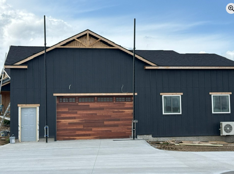 Dark blue building with wooden garage door, windows, and light poles against a blue sky.