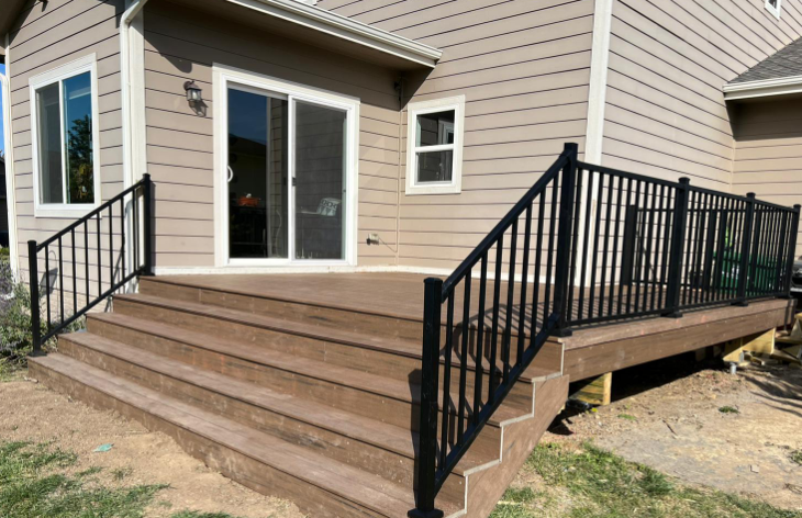 A new deck with brown composite boards and black railings, attached to a beige house, with a sliding glass door.