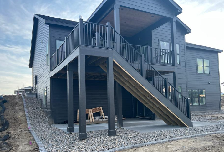 Black house with two-story deck and stairs, gravel patio, and hillside.