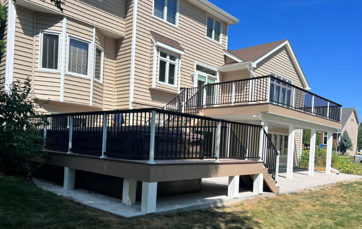 Two-story house with a deck. The deck has black railings, glass panels, and a tan base, overlooking a lawn.