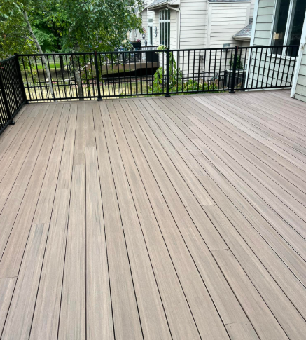A spacious, light-brown composite deck with black metal railing.