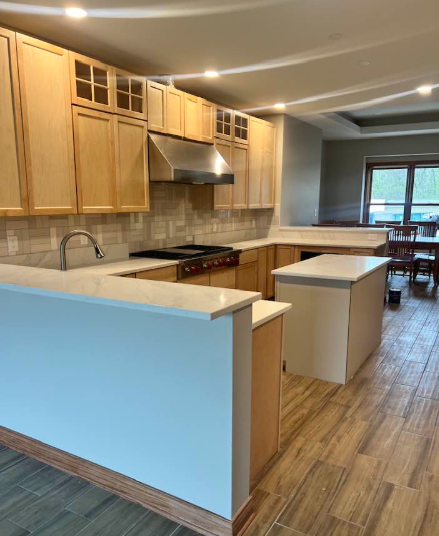 Light wood kitchen with countertops, stainless steel hood, and island; dining area visible.