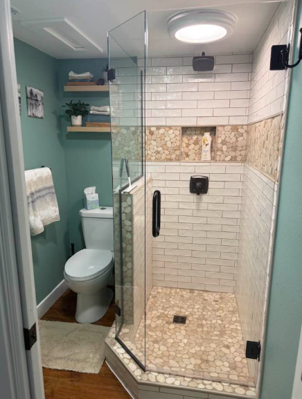 A small bathroom with a glass shower, toilet, and teal walls. White subway tile in the shower.