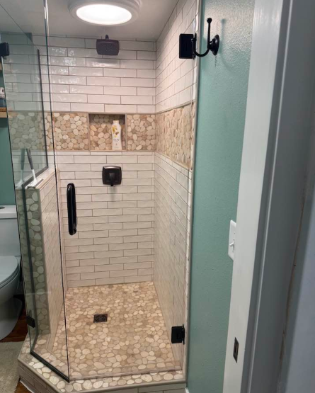 Shower with glass door, white and tan tiles, black fixtures, and light blue wall.