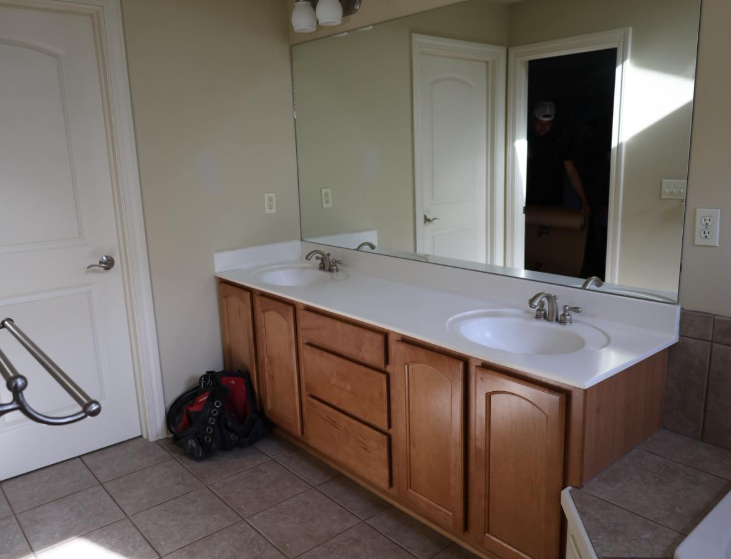Bathroom with double vanity, large mirror, and closed door. Tan cabinets and tile floor.