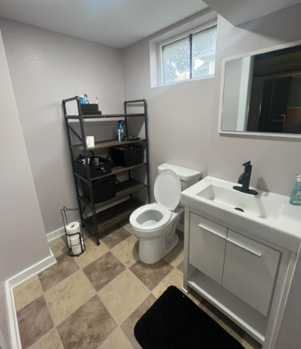 A small bathroom with a toilet, sink, shelving unit, and checkered floor.