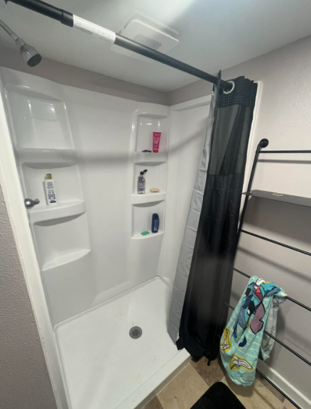 White shower stall with shelves and black shower curtain. Towel rack on the right.