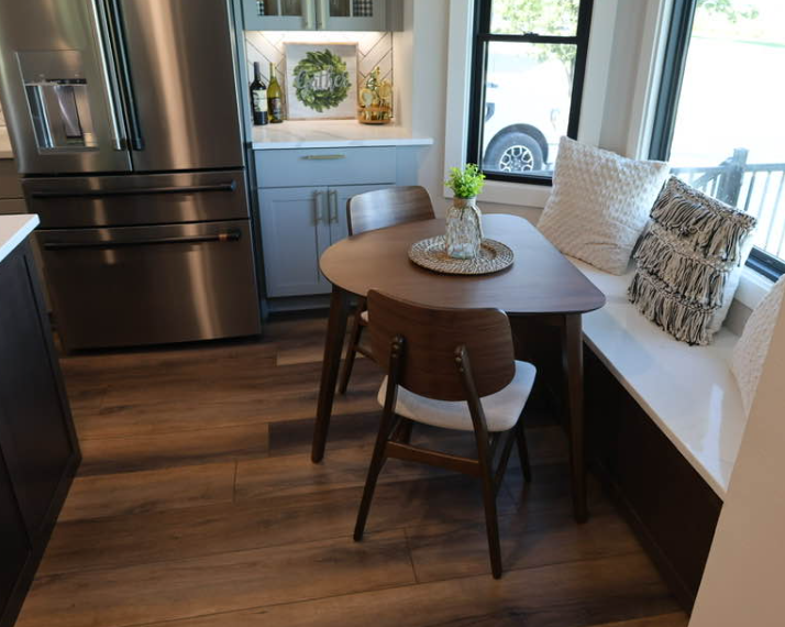 Kitchen with a triangular table, two chairs, a stainless steel refrigerator, and a window seat with cushions.