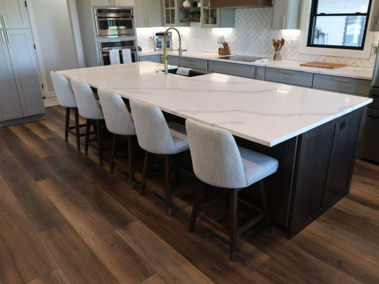 Modern kitchen with large island, seating, white countertops, dark cabinets, and wood flooring.