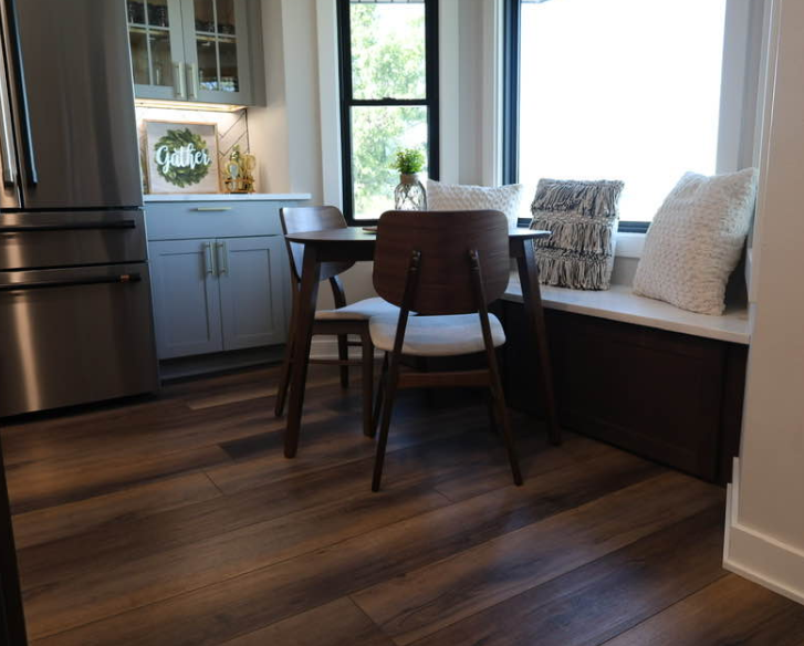 Kitchen with wooden floor, table and chairs by a window seat with pillows.