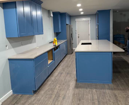 Blue kitchen cabinets and island with gray countertops in a room.