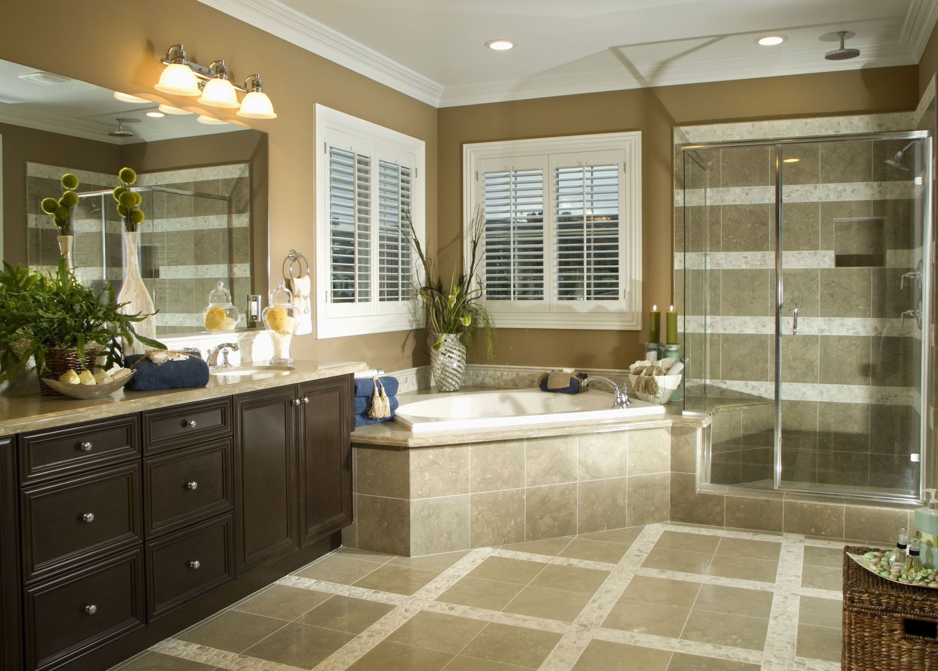 Luxurious bathroom with dark brown cabinets, beige tile, a shower, tub, and shuttered windows.