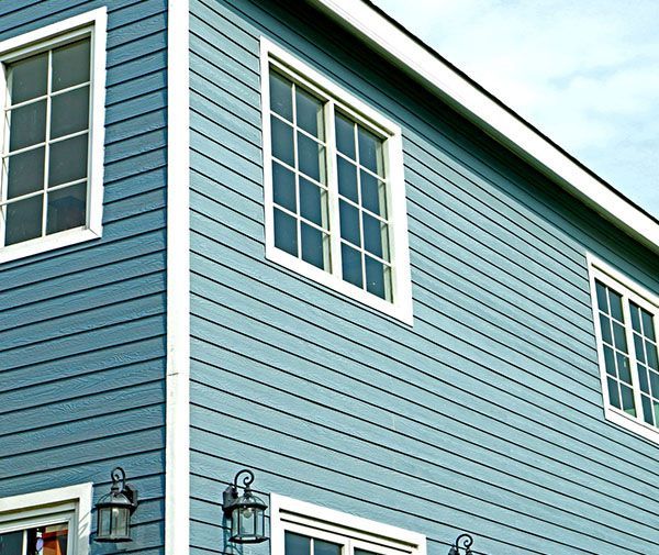 Blue siding on a house with white-framed windows, corner view.