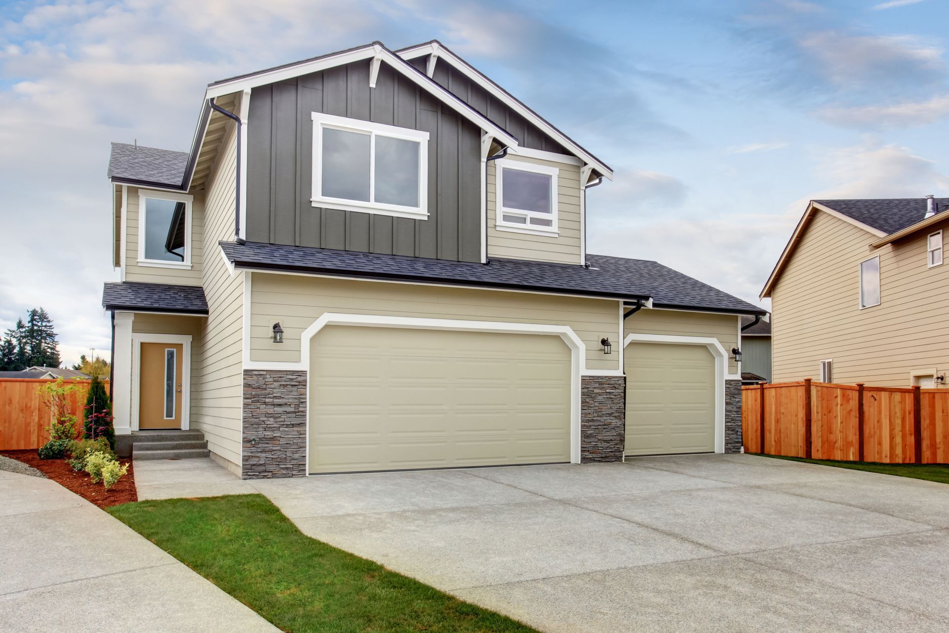 Beige two-story house with a three-car garage and stone accents, set against a blue sky.