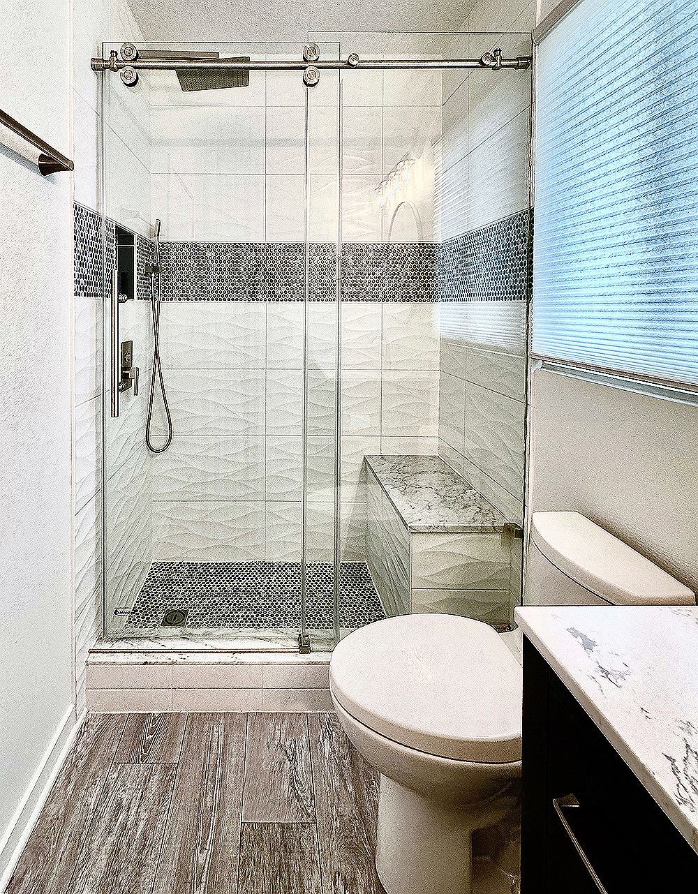 Bathroom with glass shower, mosaic tile, toilet, and marble-look vanity.