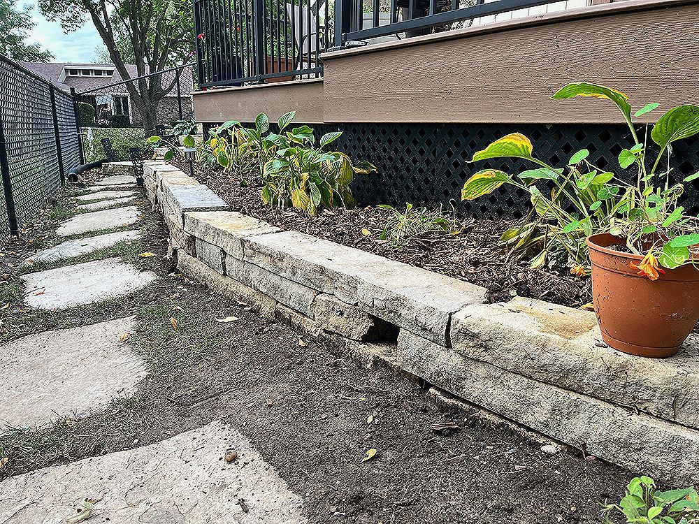 Stone retaining wall with plants and a terracotta pot near a building.