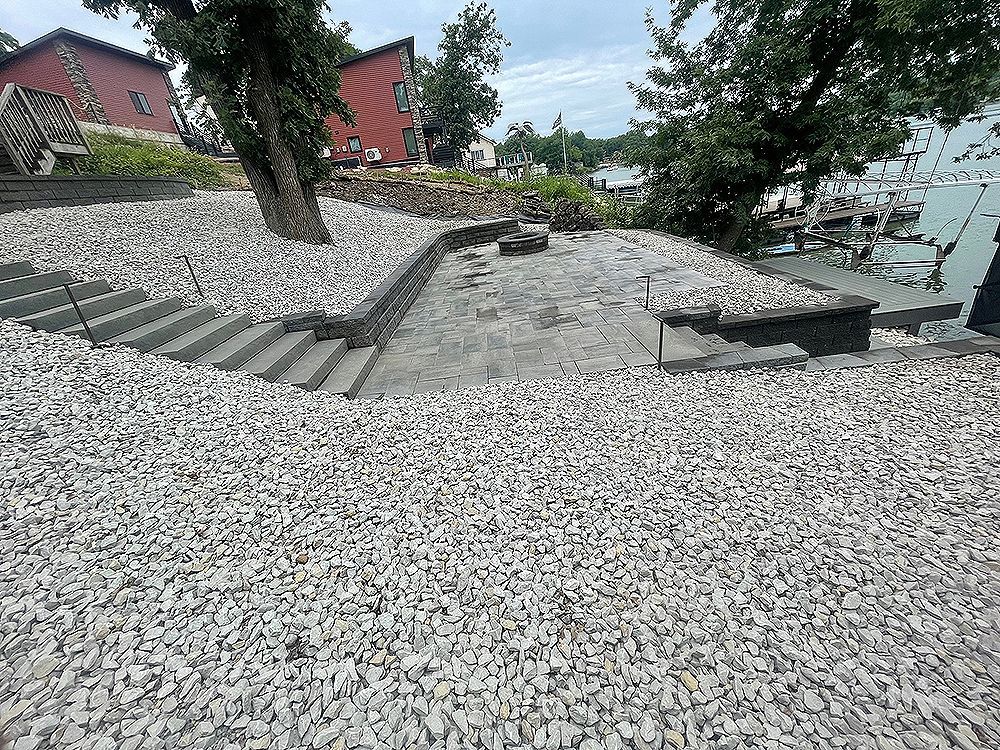 A sloped landscape covered in white rocks with concrete steps leading to a landing. Trees and buildings are in the background.