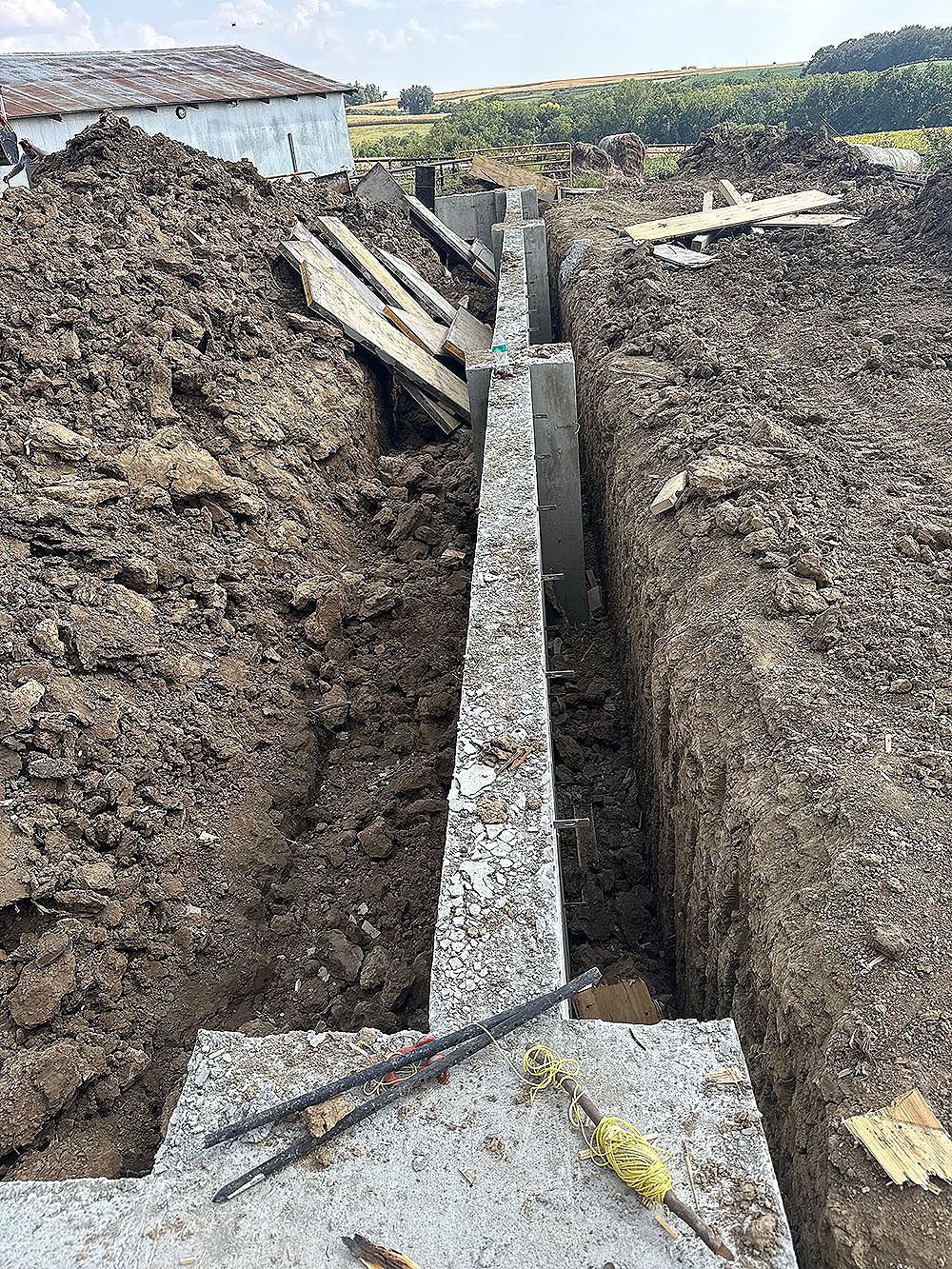 Construction site: a concrete foundation with rebar lies in a deep trench surrounded by dirt.