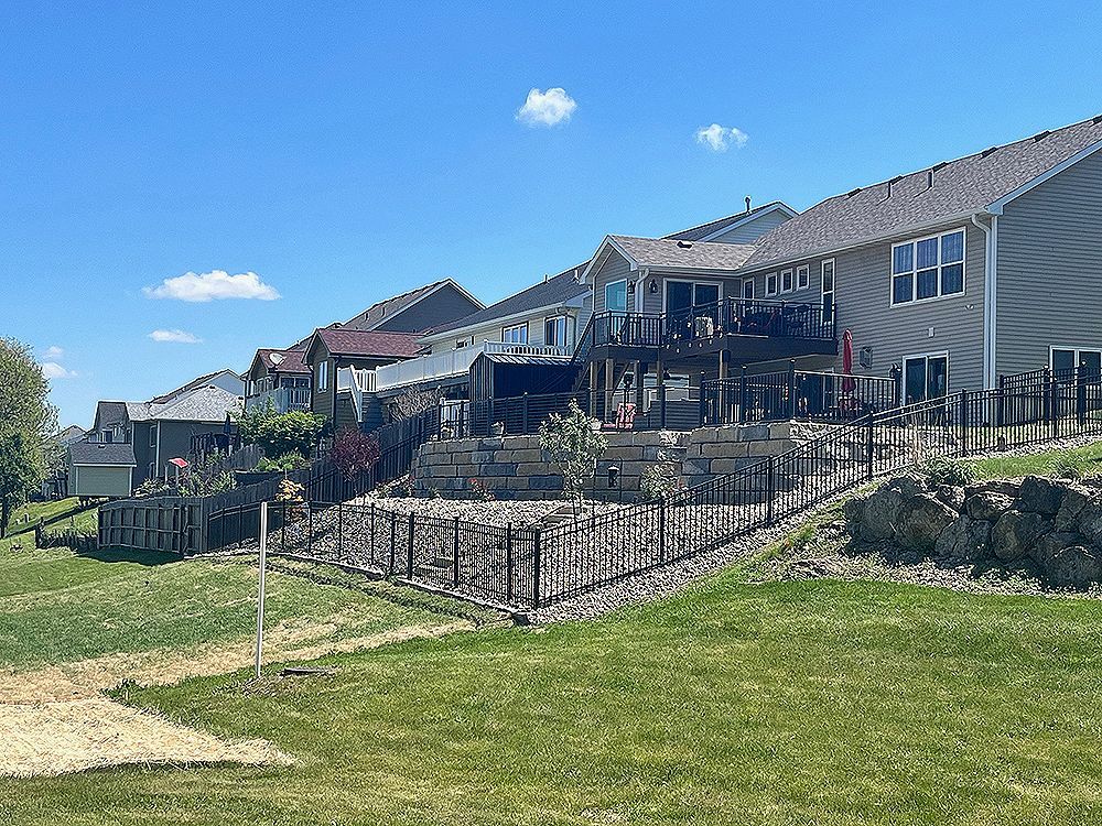 Row of houses with decks on a grassy hillside under a blue sky with scattered clouds.
