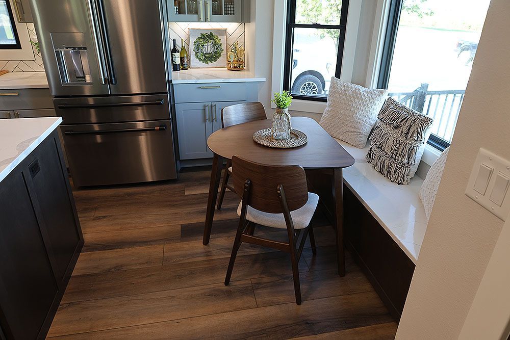 Kitchen with a small, triangular table and two chairs near a window seat with pillows.