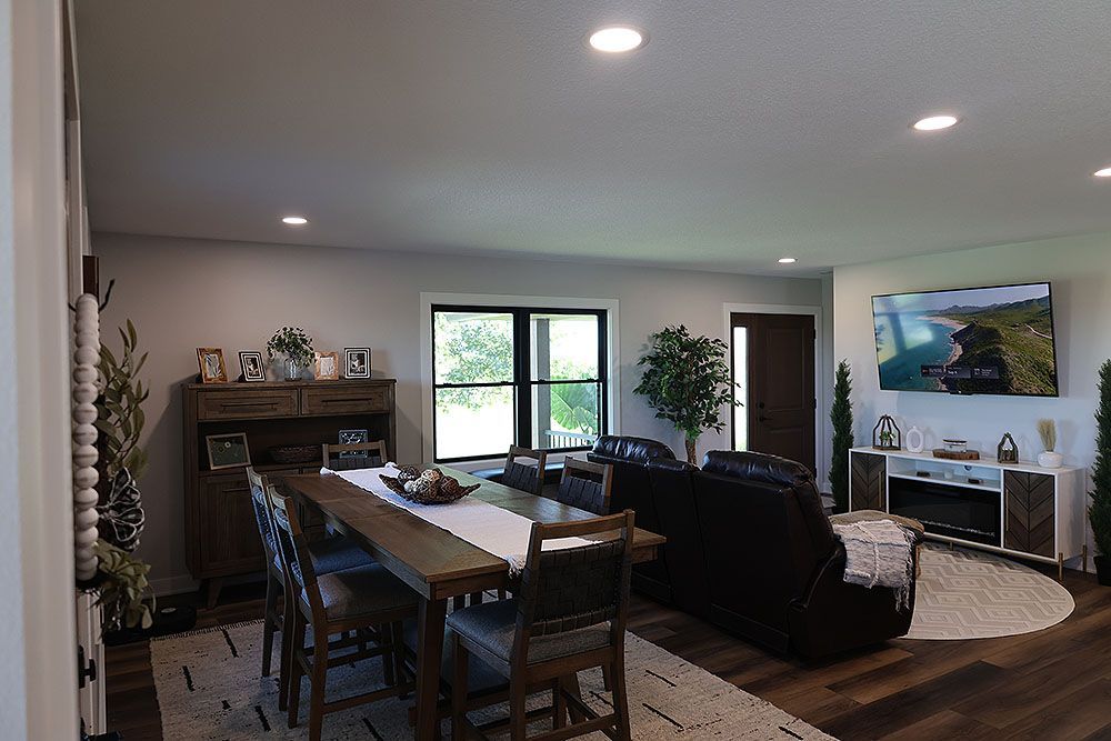 Spacious living area with dining table, dark wood floors, large windows, and a mounted TV.