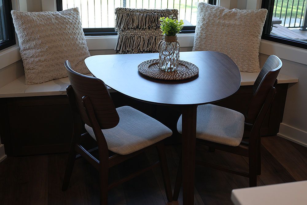 A small, dark wooden dining table with two chairs, set in a bay window nook, with pillows.