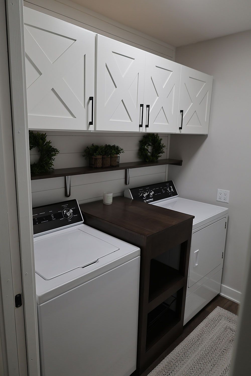 Laundry room with white washer/dryer, white cabinets, and dark wood countertop/shelves.