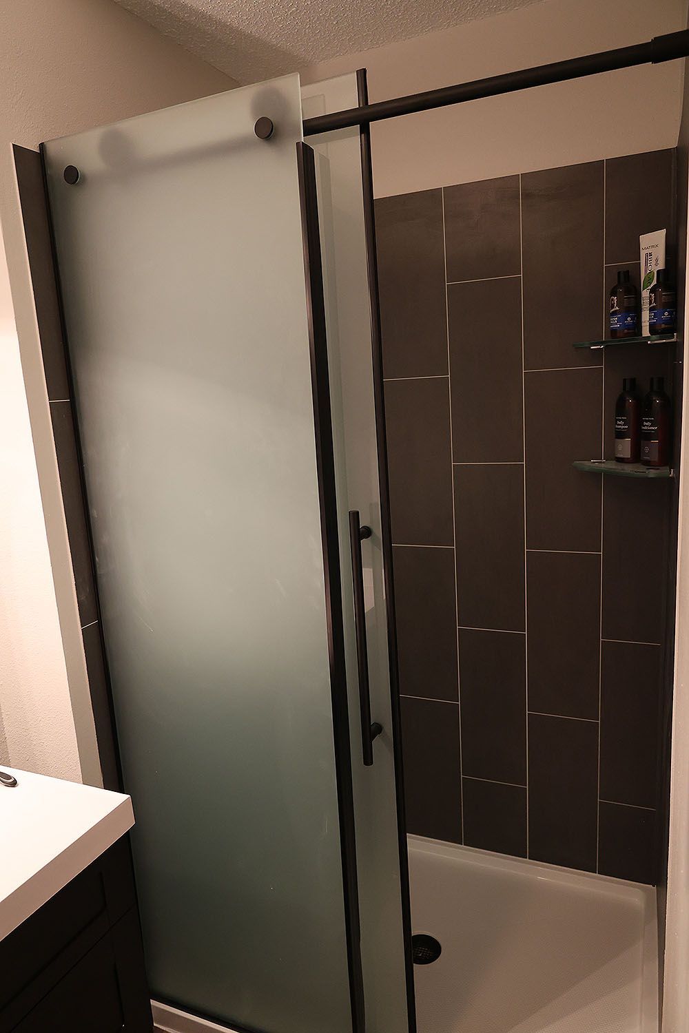 Shower with frosted glass door, dark tile, and black fixtures in a modern bathroom.