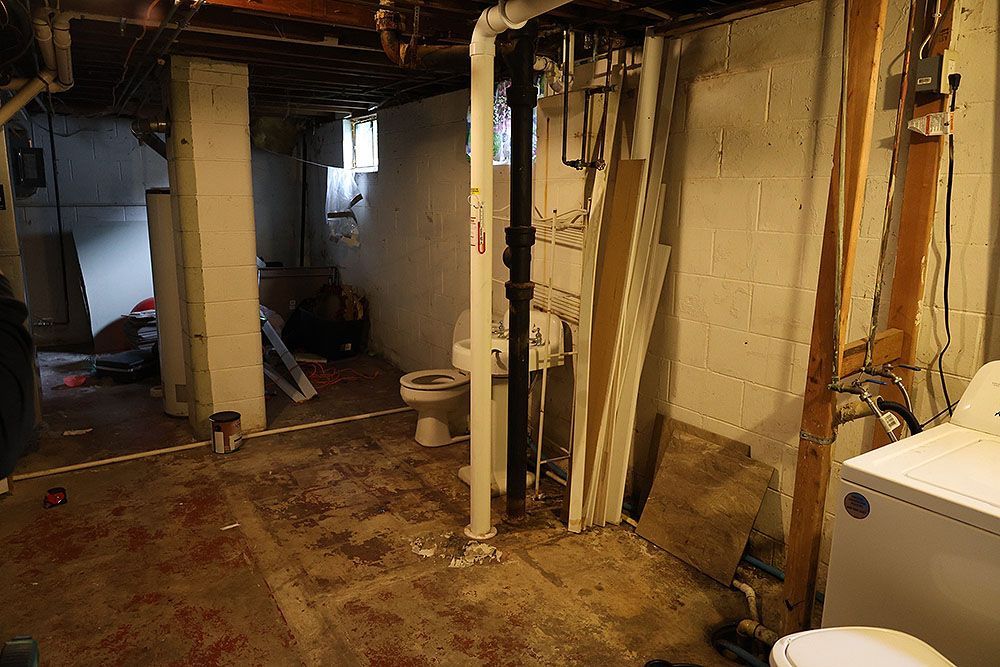 Basement interior with exposed pipes, unfinished walls, a toilet, and a washing machine.
