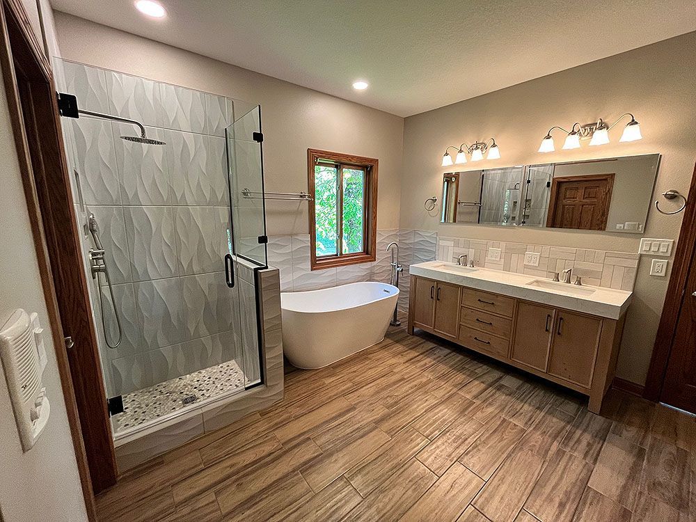 Spacious bathroom with glass shower, freestanding tub, double vanity, and wood-look tile flooring.