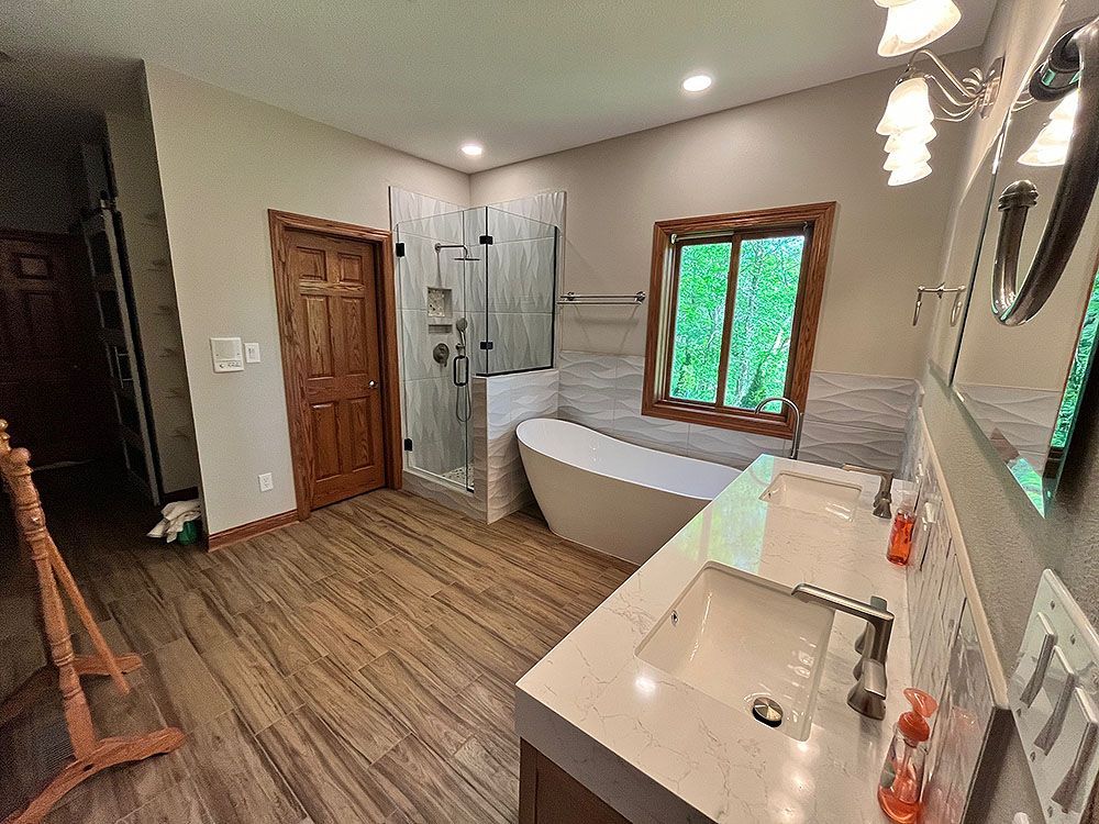 Bathroom with a wooden door, shower, bathtub, and double vanity. The floor and trim are wood.