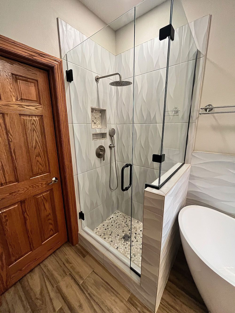 Modern bathroom with a glass shower enclosure, wood door, and a freestanding tub.