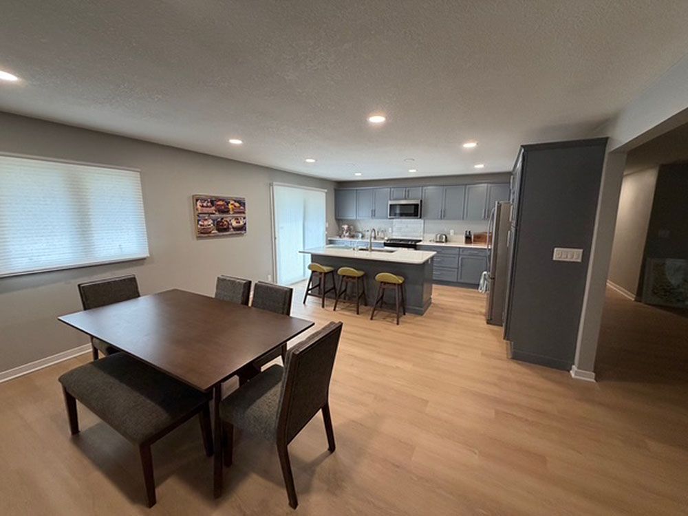 Dining area with table, chairs, and bench, connected to kitchen with island and gray cabinets.