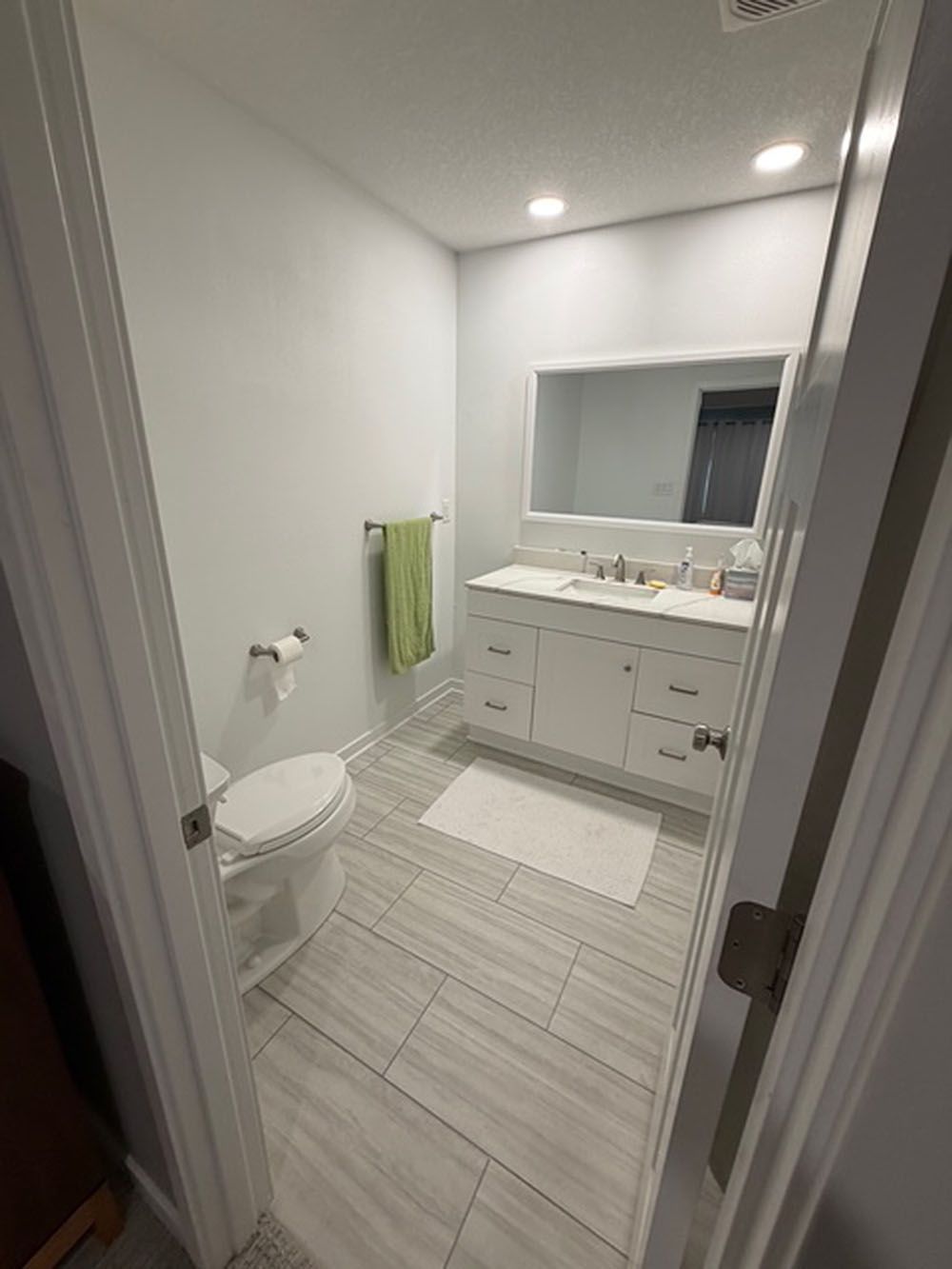 Bathroom with white vanity, toilet, light gray floor tiles, and a green towel.