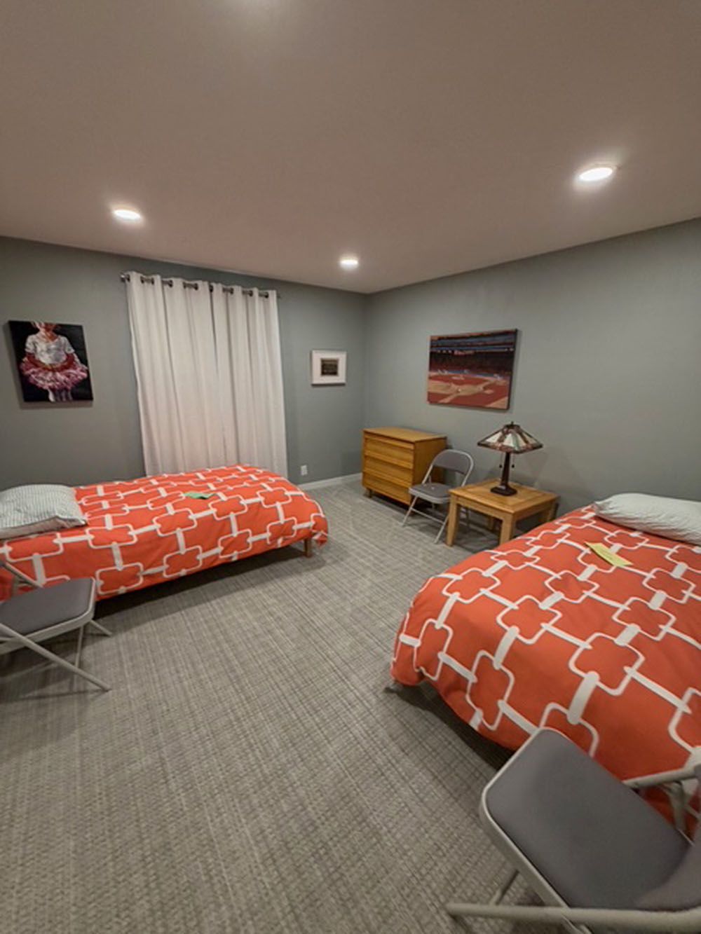 Two beds with orange and white patterned bedding in a gray-walled room.  Two gray chairs are next to the beds.
