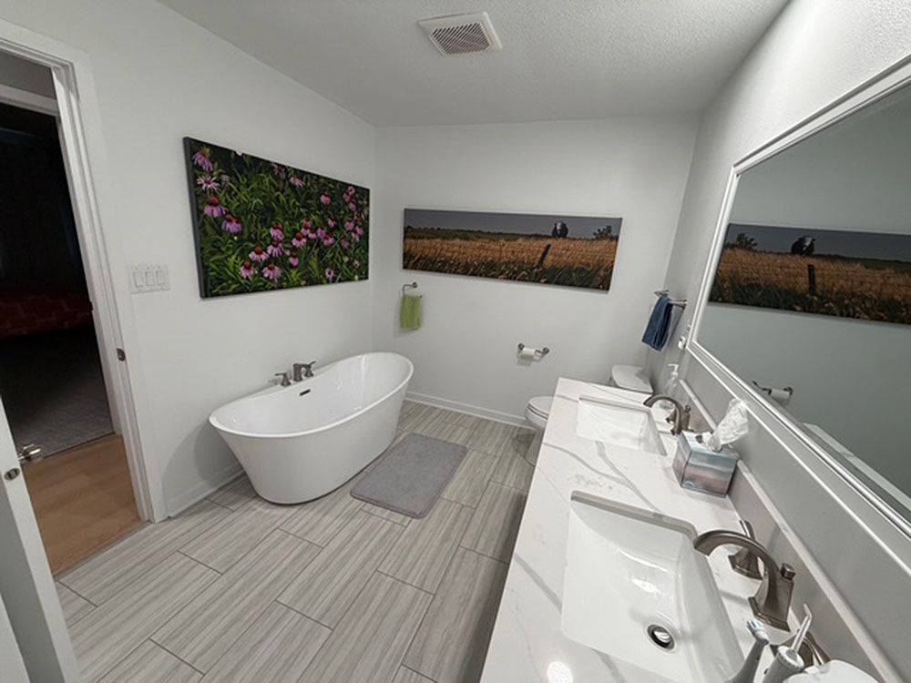 Bathroom with a white freestanding tub, double vanity, and floral artwork. Gray and white color scheme.