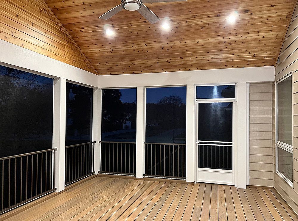 Screened porch with wooden ceiling and floor, three windows, and black railings, at dusk.