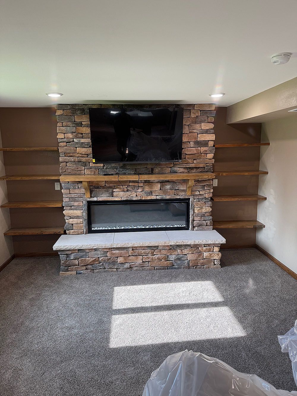 Fireplace with stone surround, built-in shelves, TV, and electric firebox in a room with carpet.