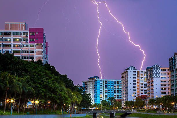 Lightning strikes over a city at dusk, illuminating buildings and a purple sky.