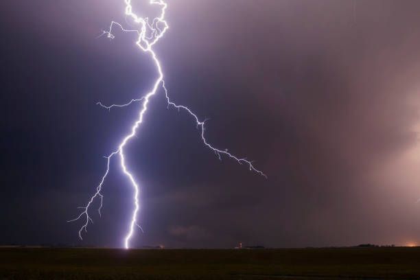 Lightning bolt strikes across a dark, stormy sky over a field.