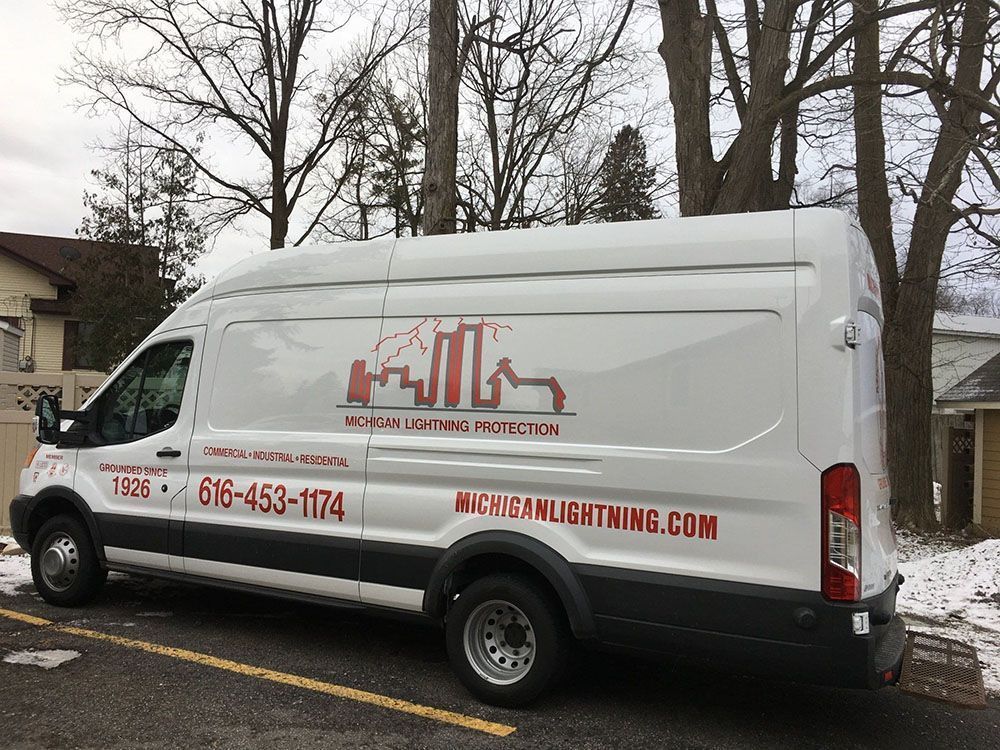 White van with red logo, "Michigan Lightning," parked outside with trees in the background.