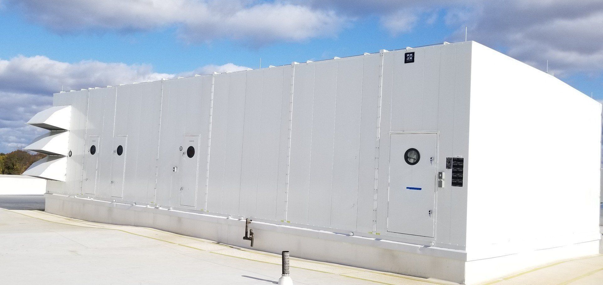 White industrial building on a rooftop with vents, circular openings, and a door. Blue sky with clouds.