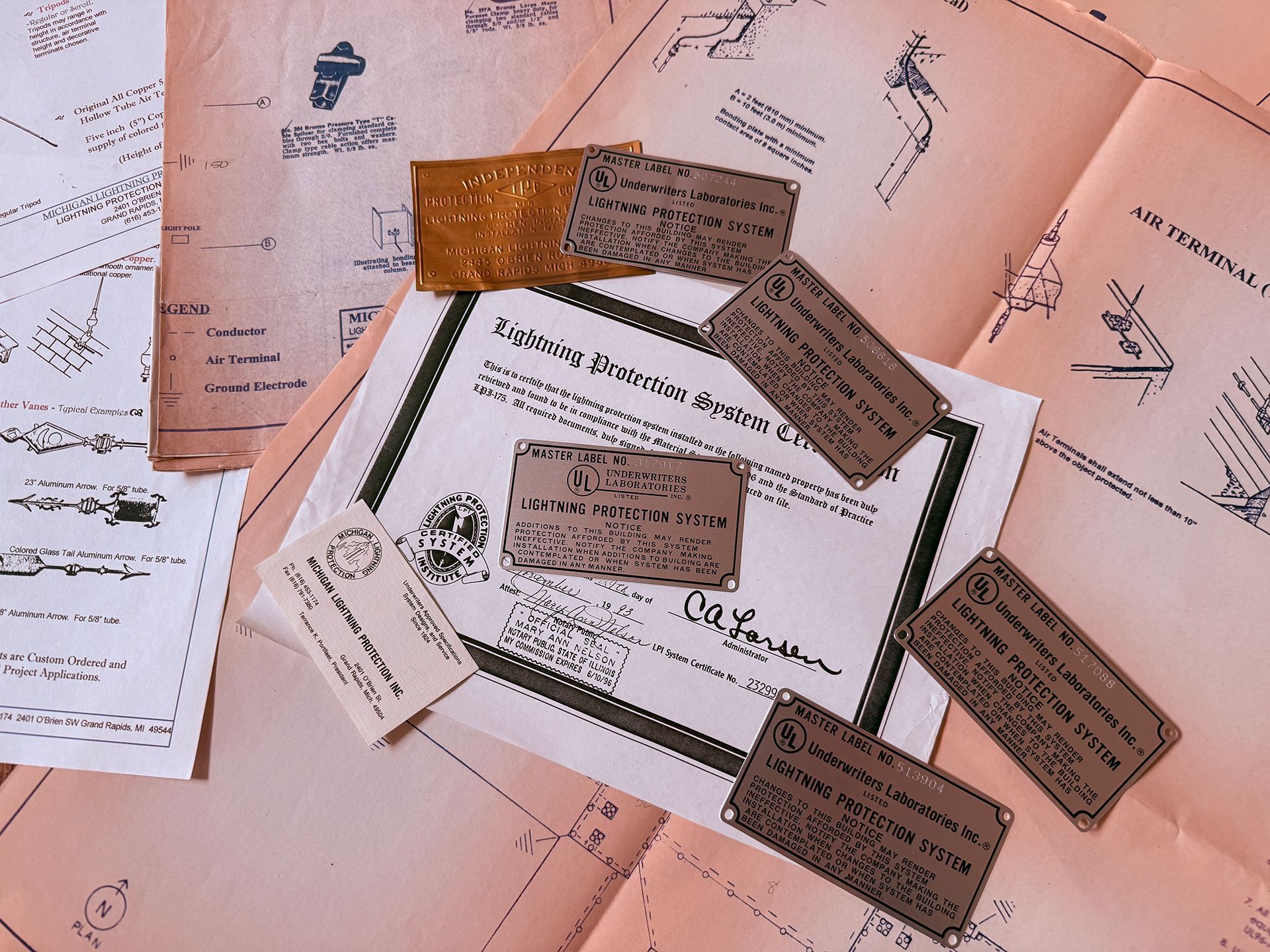 Technical blueprints and diagrams spread out with several vintage metal identification plates and a paper document.