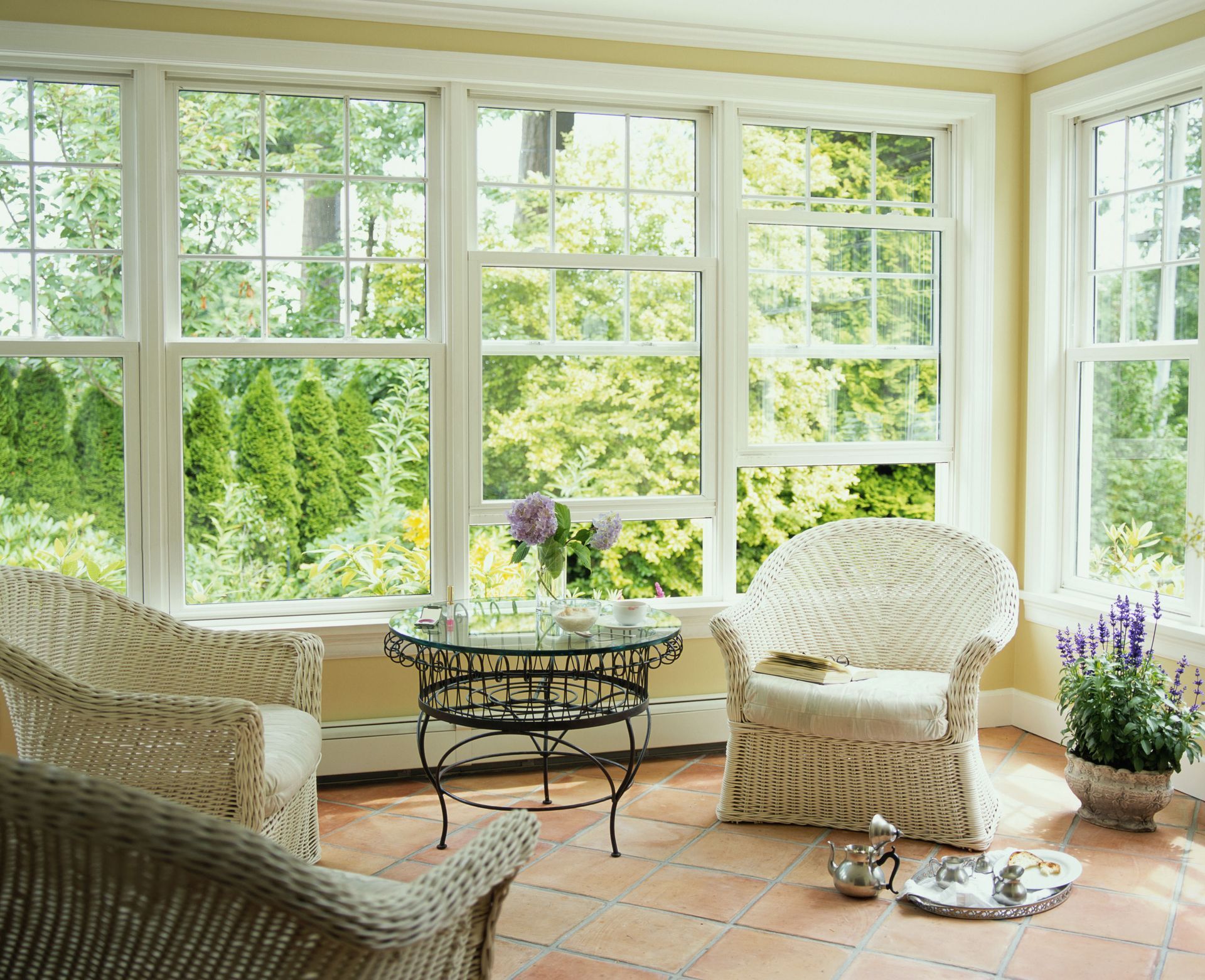 Sunroom with wicker chairs, a table, and large windows overlooking a garden.