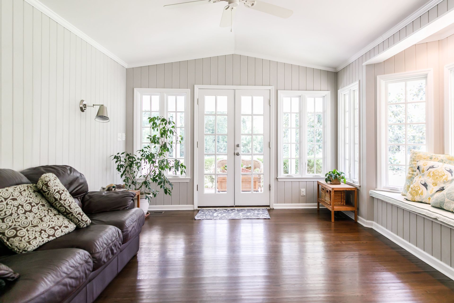 Living room with gray paneled walls, French doors, dark wood floor, and brown leather sofa.